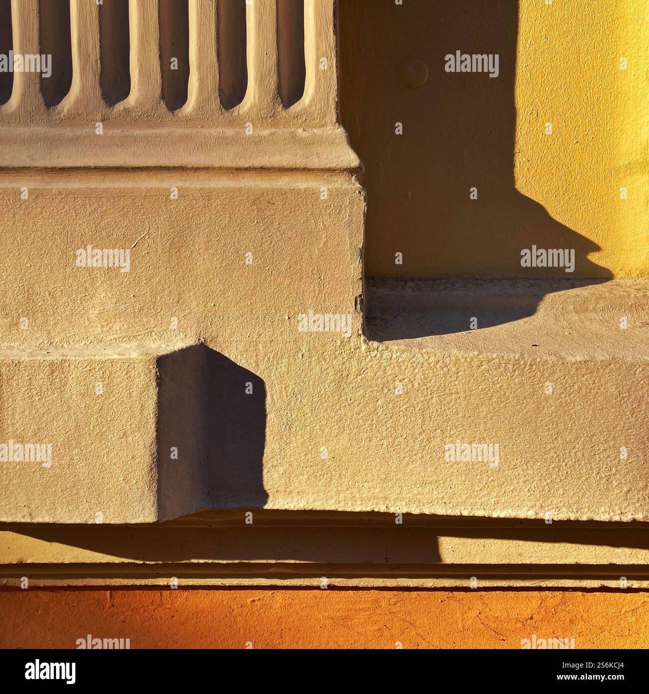 Colorful architectural abstraction featuring a yellow wall with shadow patterns and orange accents with warm tones and geometric themes under the sun. - Smartphone Captured Stock Image