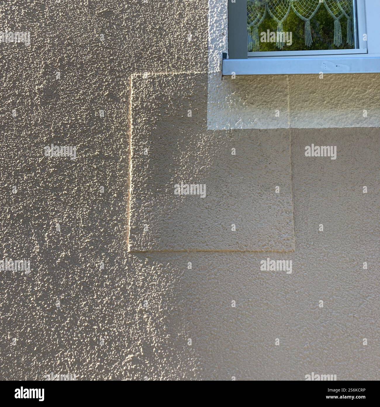 Detail of a textured building exterior wall, above a portion of a window with ornaments inside. - Smartphone Captured Stock Image