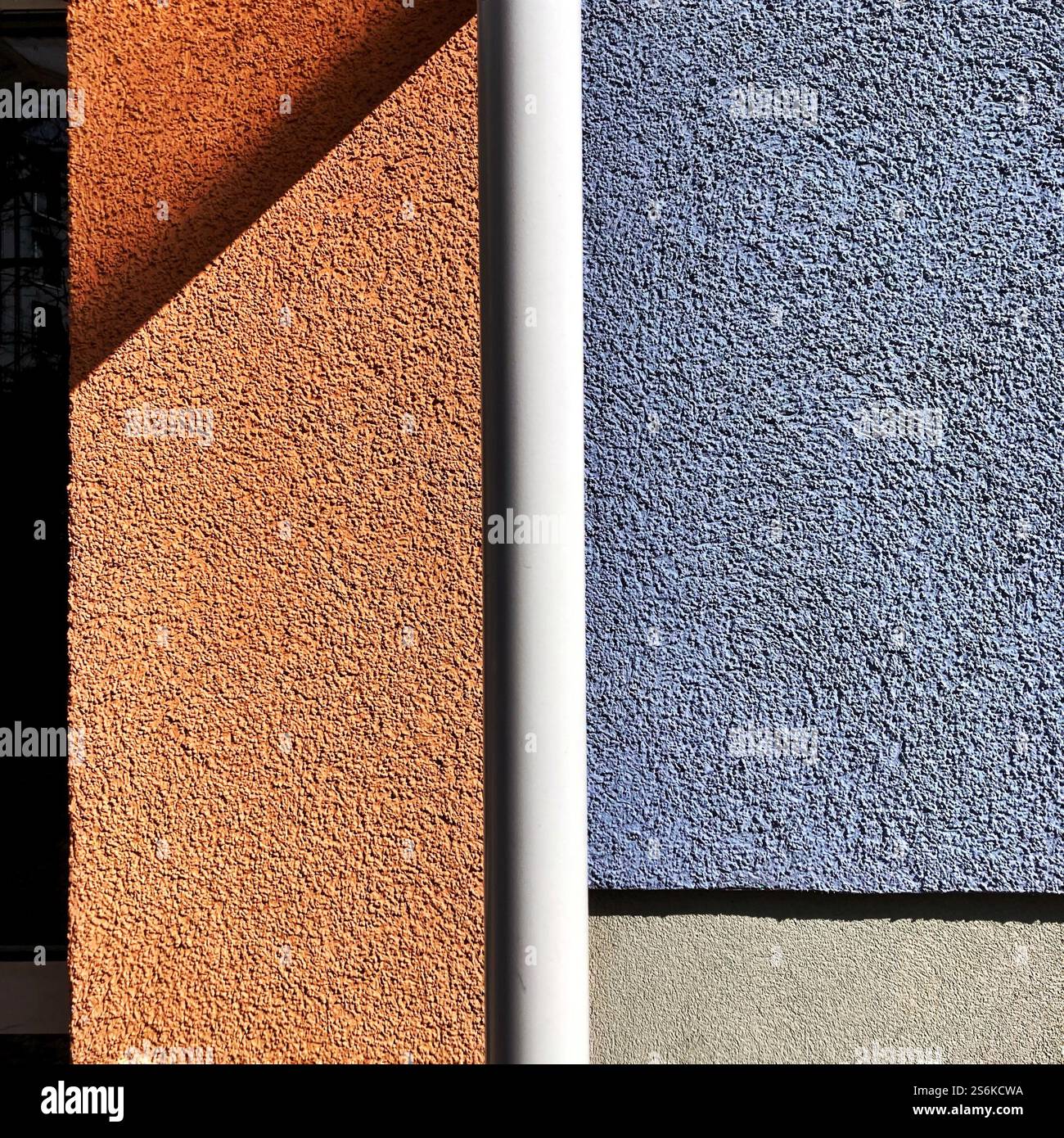 Vivid contrast of orange and blue textured wall surfaces divided by a vertical white pipe in daylight, creating a minimalist geometric ambience. - Smartphone Captured Stock Image