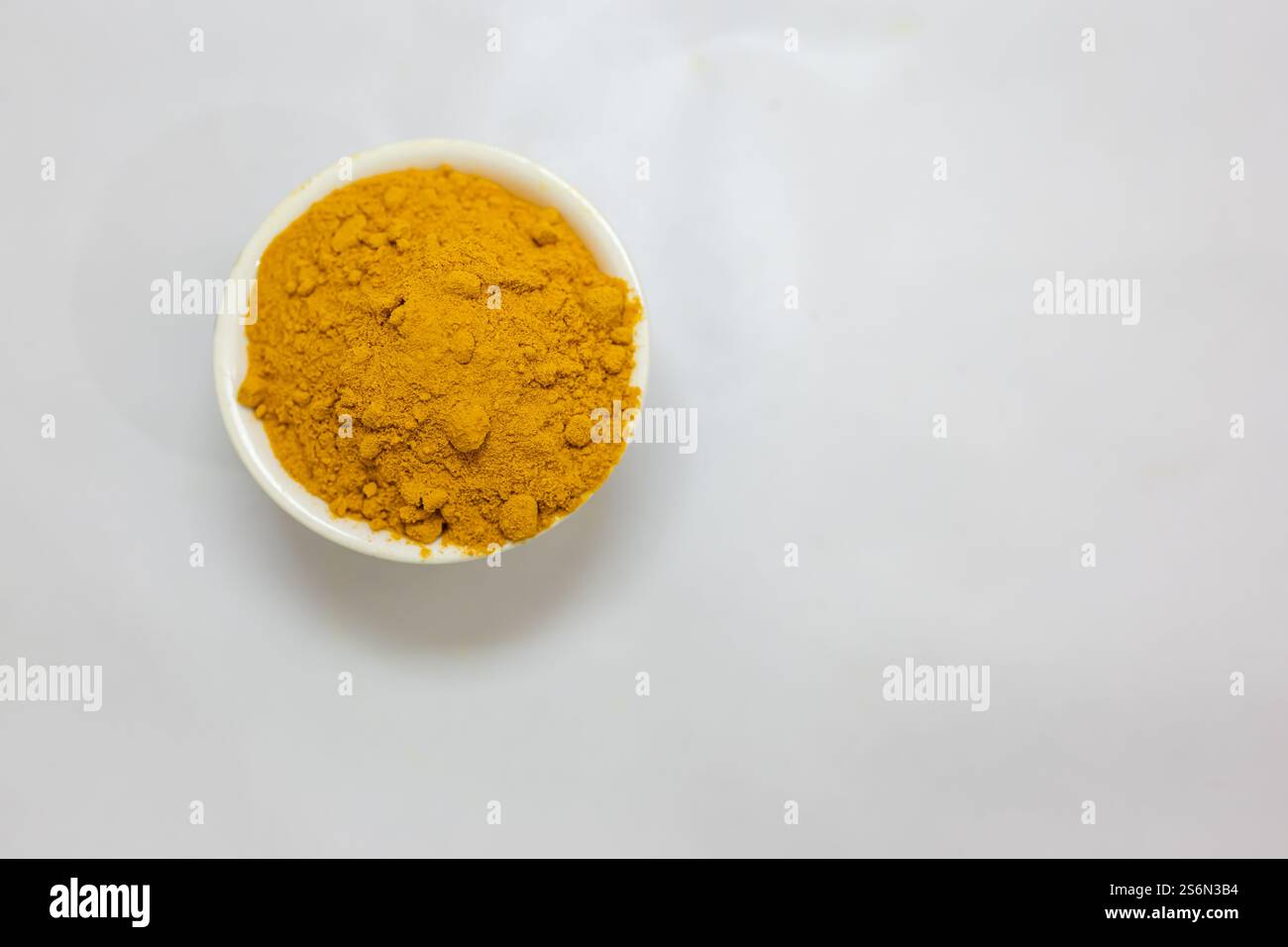 Fresh turmeric powder in ceramic bowl with blurred white Background studio shot Stock Photo