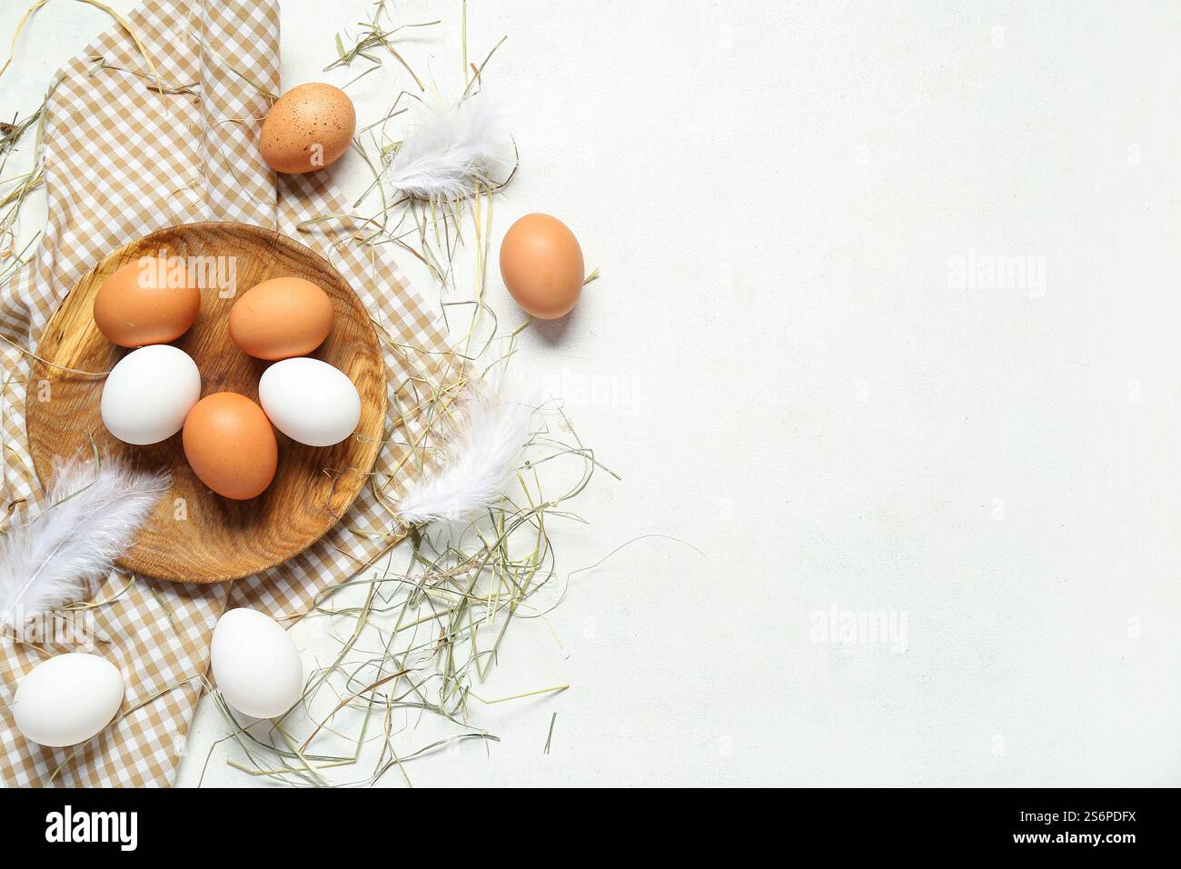 Wooden plate with raw chicken eggs and feathers on white background ...