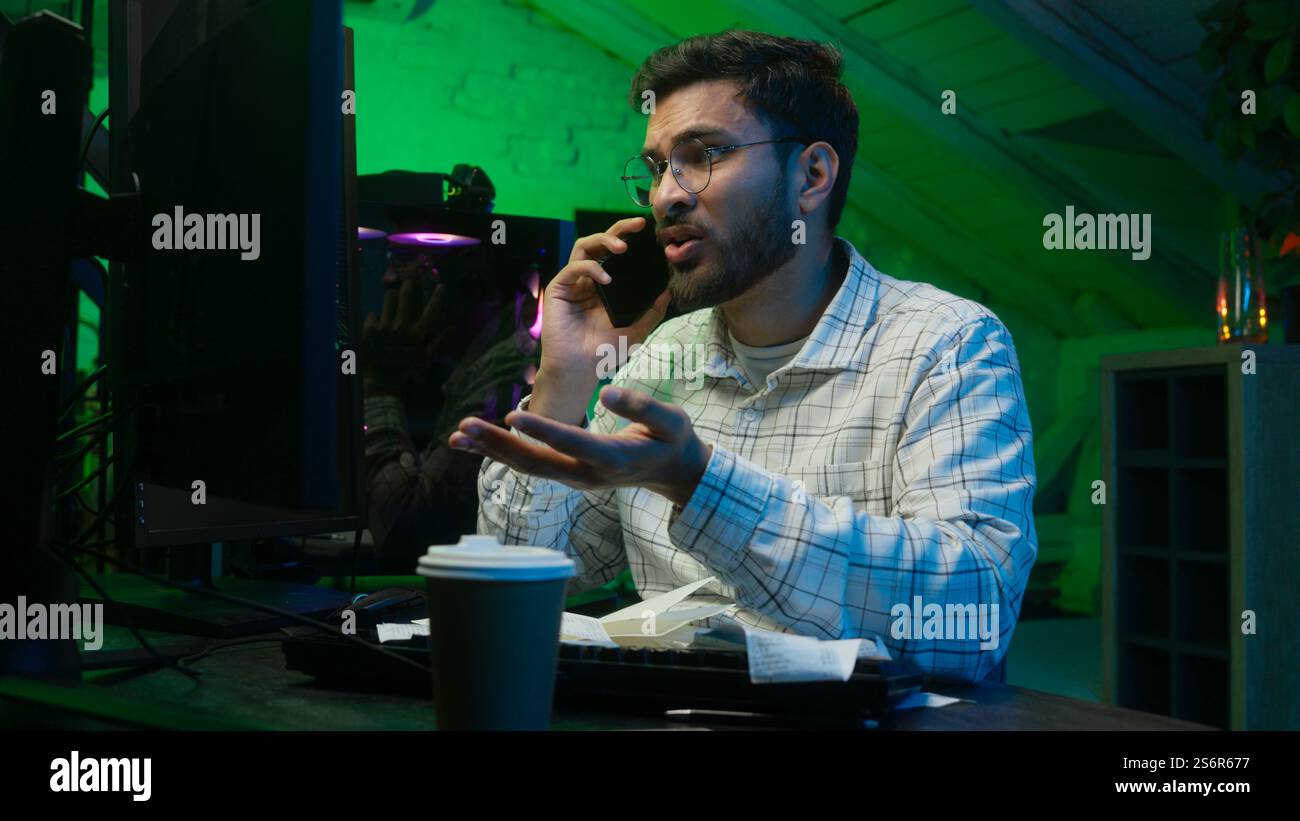 Stressed Arabian Indian man male guy looking code coder programmer technology talk mobile phone error hacker problem loss worker computer trouble IT Stock Photo
