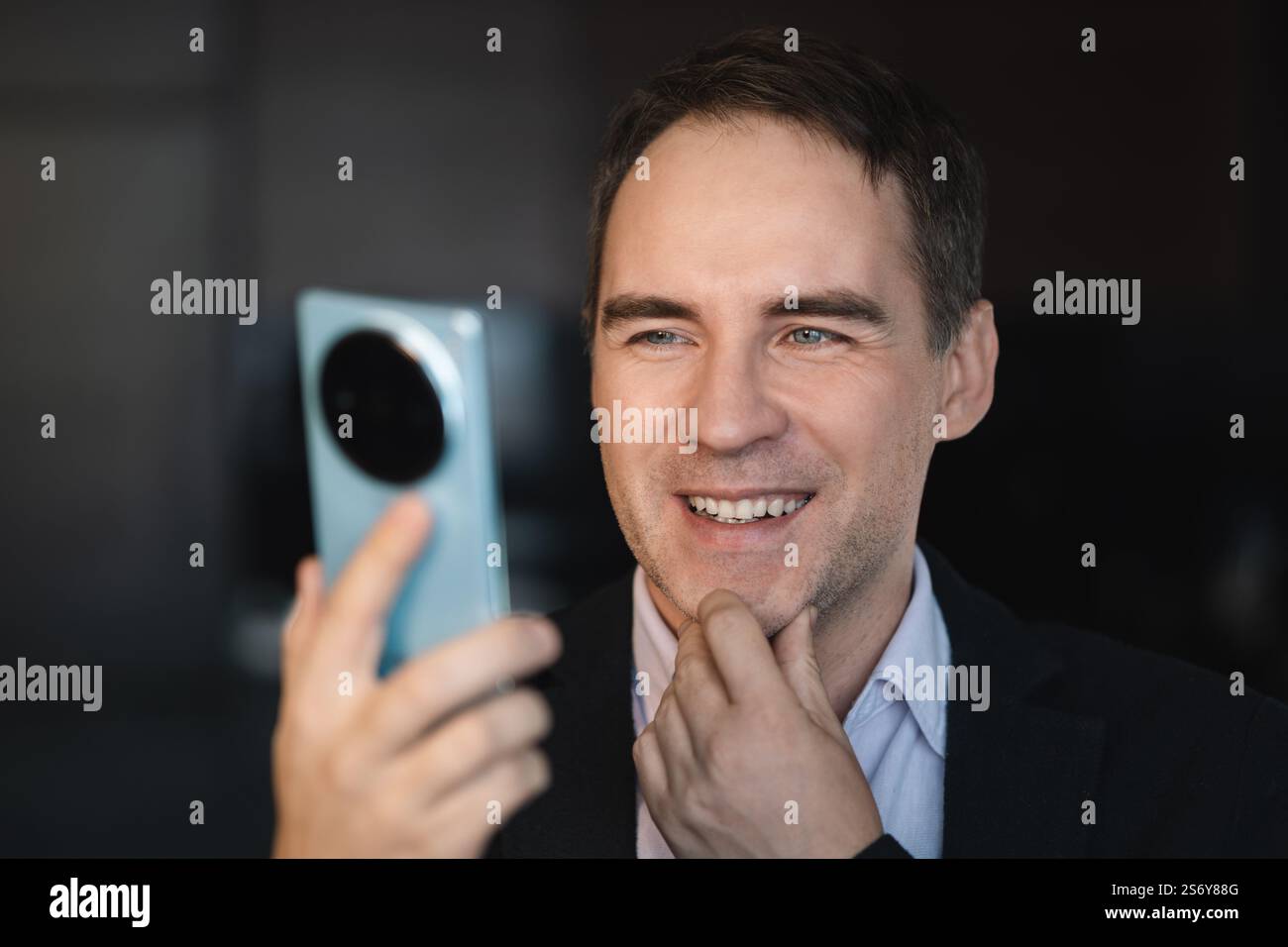 Businessman texting on his mobile phone sitting entering data with his thumbs and concentrating on screen Stock Photo