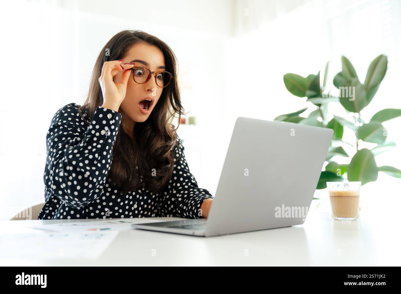 Surprised business woman with glasses looking at a laptop screen with ...