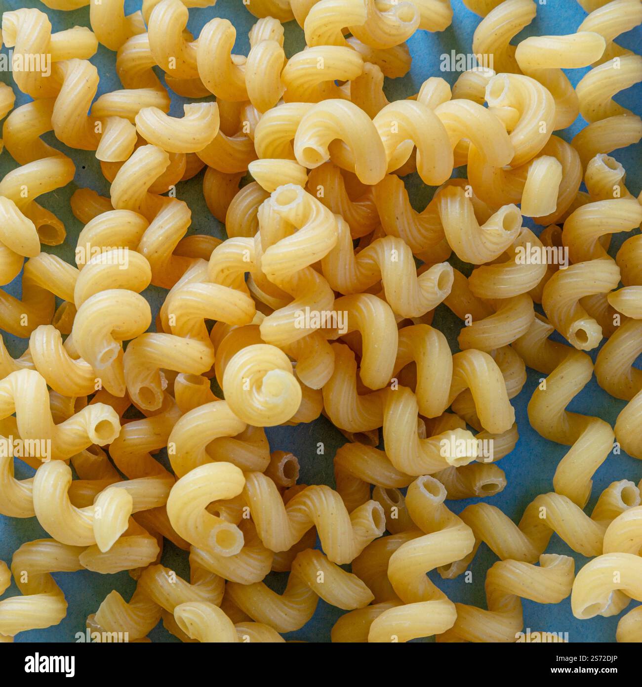 A detailed close-up image of uncooked spiral pasta showcasing their intricate texture and bright yellow color, placed on a light vibrant background. Stock Photo