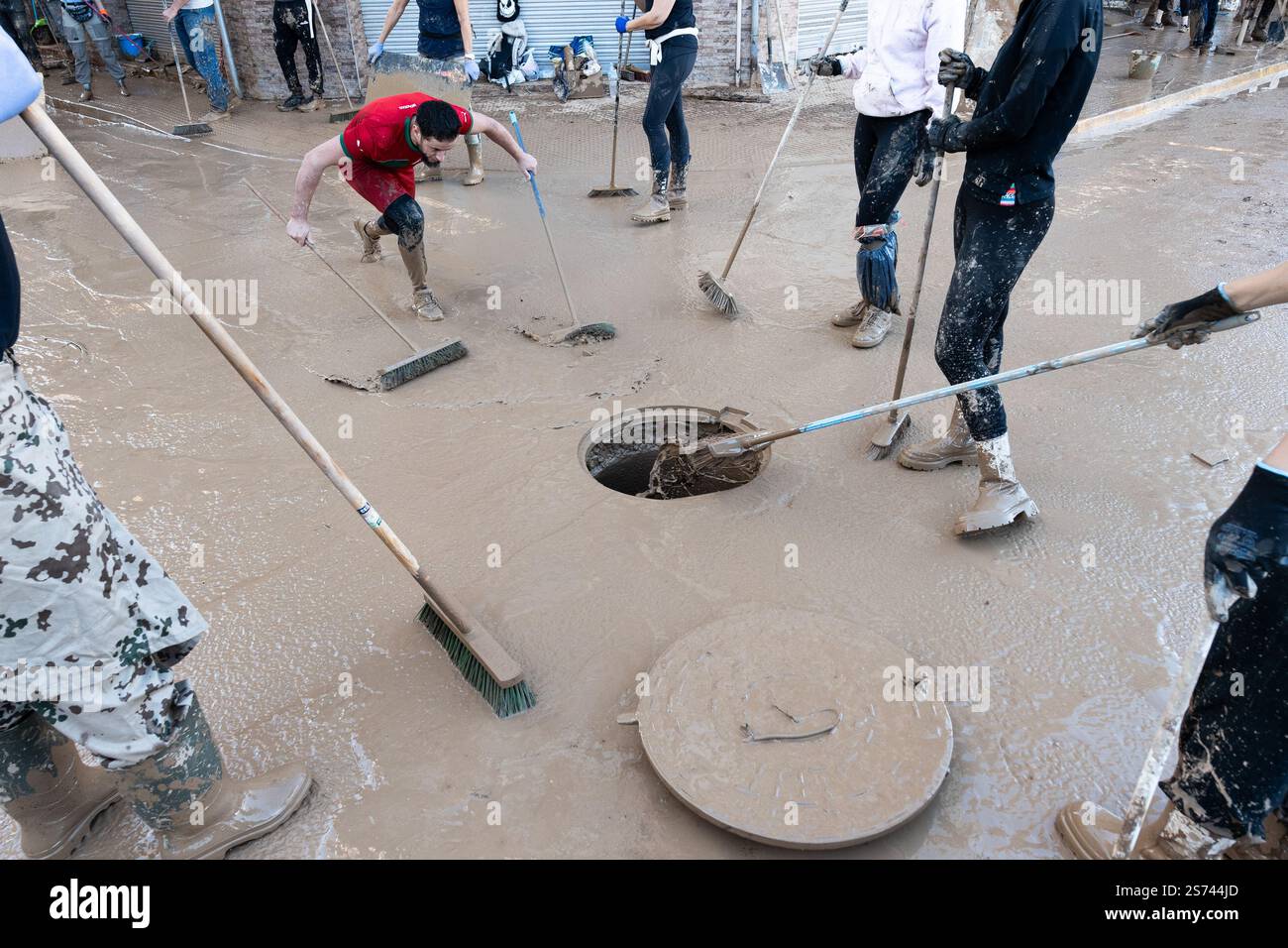 People sweeping and removing mud from the streets to a manhole cover after DANA flooding. Alfafar, Spain. Stock Photo