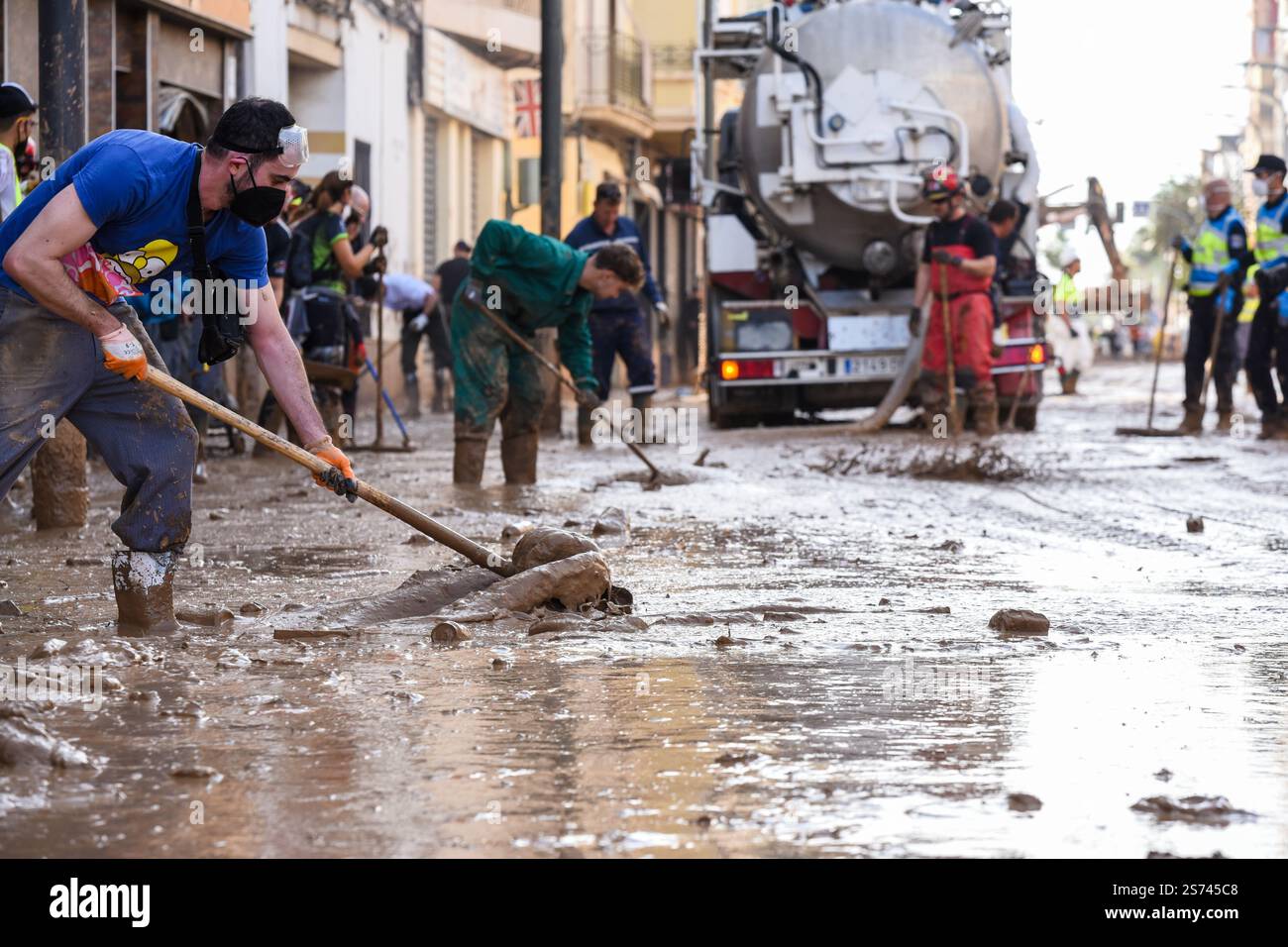 People cleaning street flooded in watery mud after DANA flooding. Natural disaster aftermath. Massanassa, Spain Stock Photo