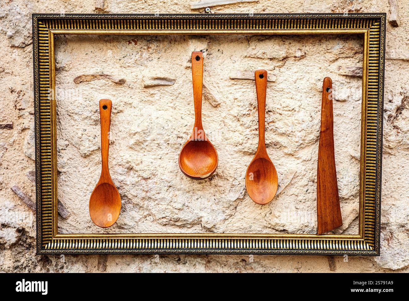 Rustic wooden utensils framed on textured stone wall. Stock Photo