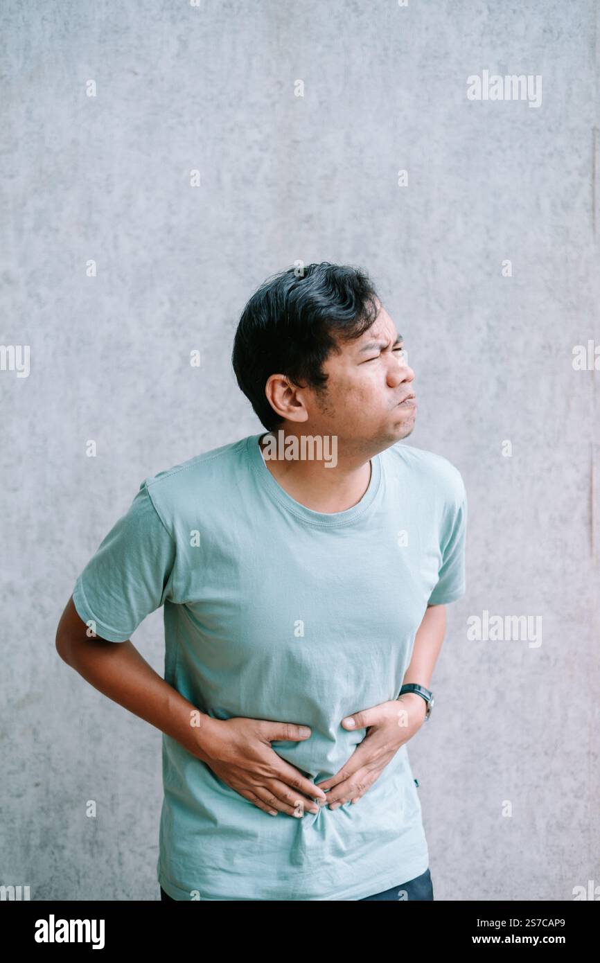 Man experiencing stomach discomfort, holding his abdomen in pain. Stock Photo