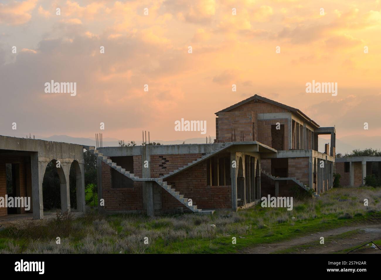 Ruins of an unfinished structure are bathed in warm light as dusk approaches, surrounded by wild grass and tranquility. Stock Photo
