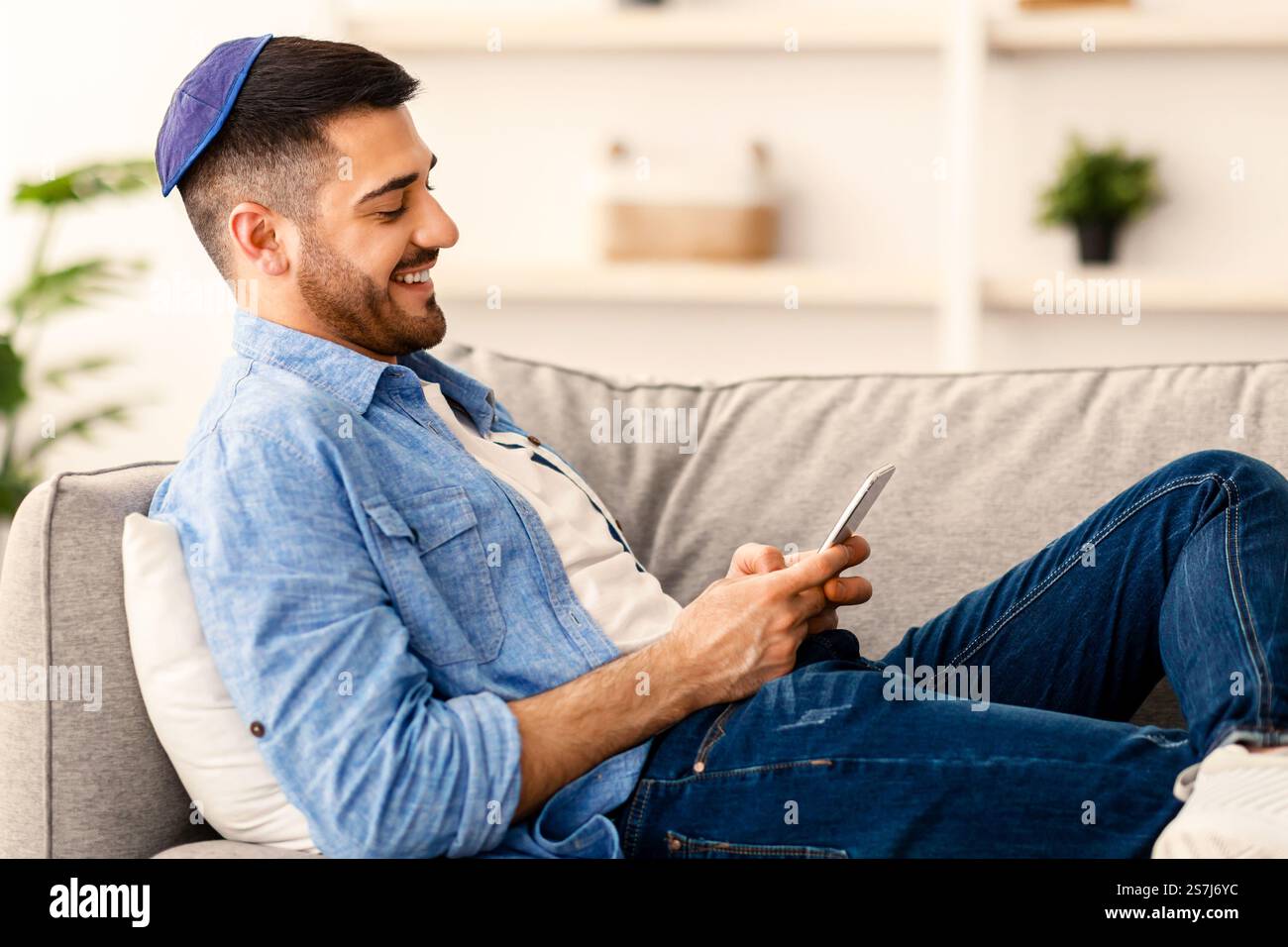 Smiling jew man using mobile phone sitting on couch Stock Photo