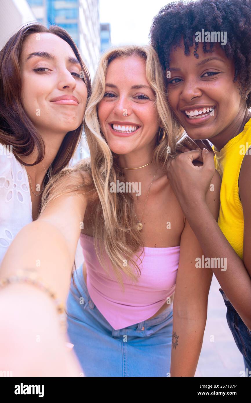 Three happy young women taking a selfie together in a city street ...