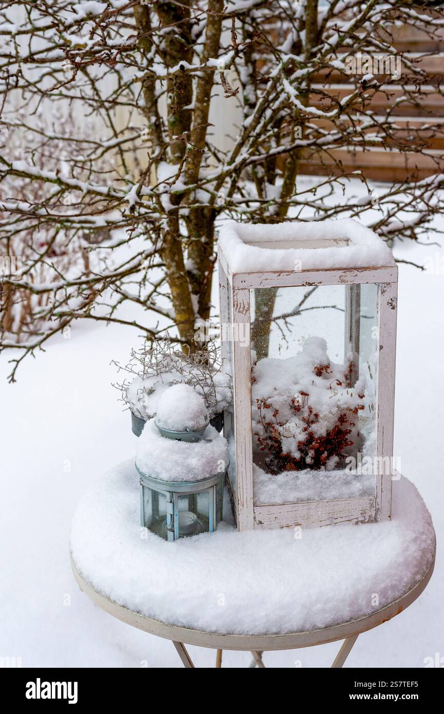 Snowy garden with a small round table, lantern, and a tree Stock Photo