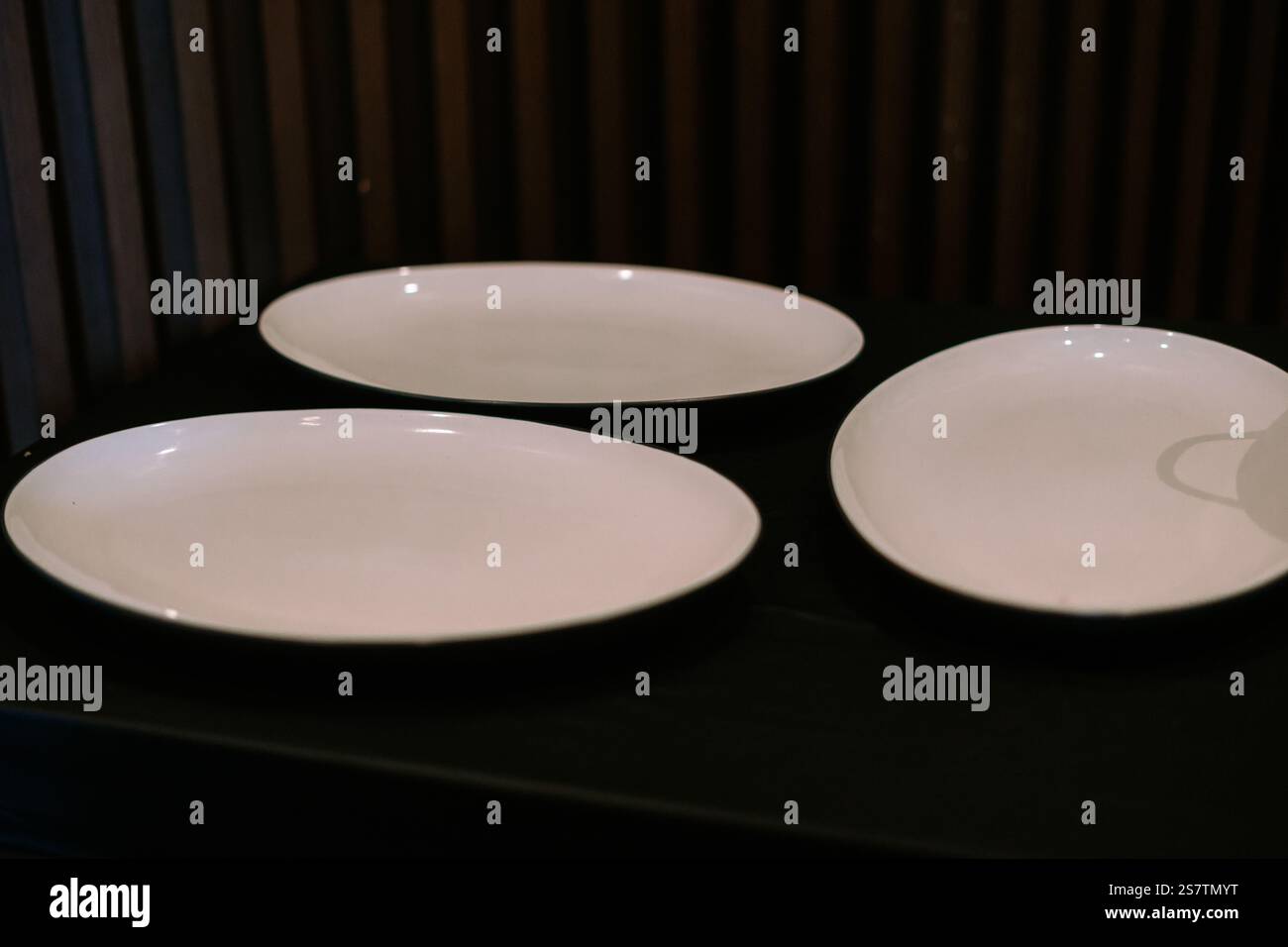 Three elegant oval white plates on a dark surface. Stock Photo