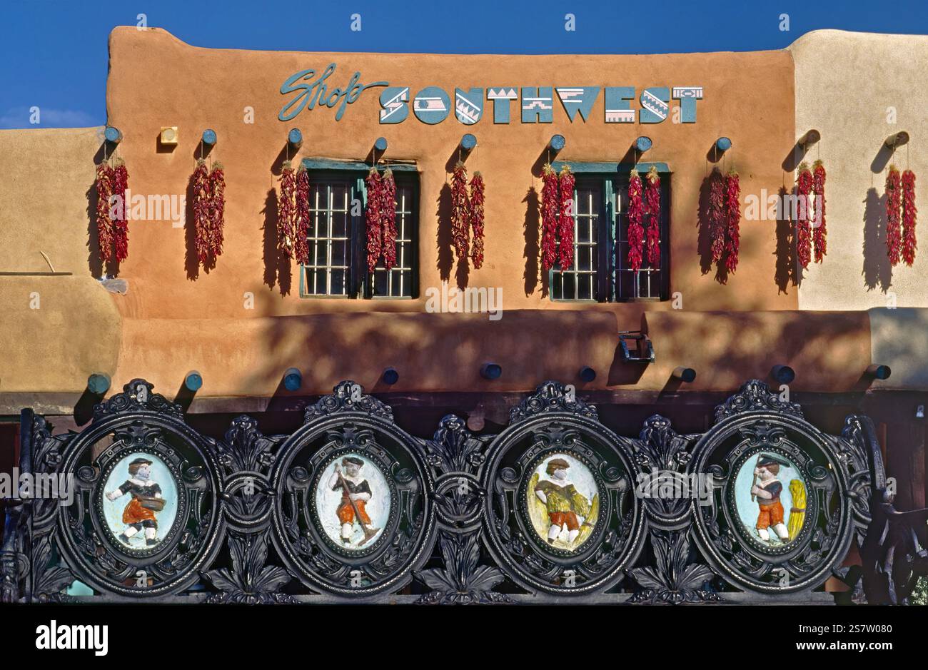 Paintings at wrought iron bench, chili pepper ristras at adobe building at Plaza in Taos, New Mexico, USA Stock Photo