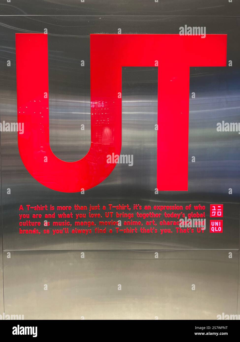 Red logo abbreviate UT,  Uniqlo T-shirts. Against a chrome slightly reflective wall. UT brand features graphic tee such as manga, design, photography. - Smartphone Captured Stock Image