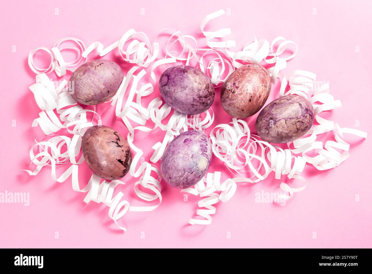 Painted eggs for Easter in white decorative nest on pink surface. Easter flat lay with copy space Stock Photo
