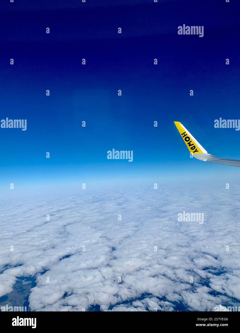 View from a window seat on a Spirit Airlines flight, showing the airplane wing with 'Howdy' written on it, set against a backdrop of clear skies. A un - Smartphone Captured Stock Image