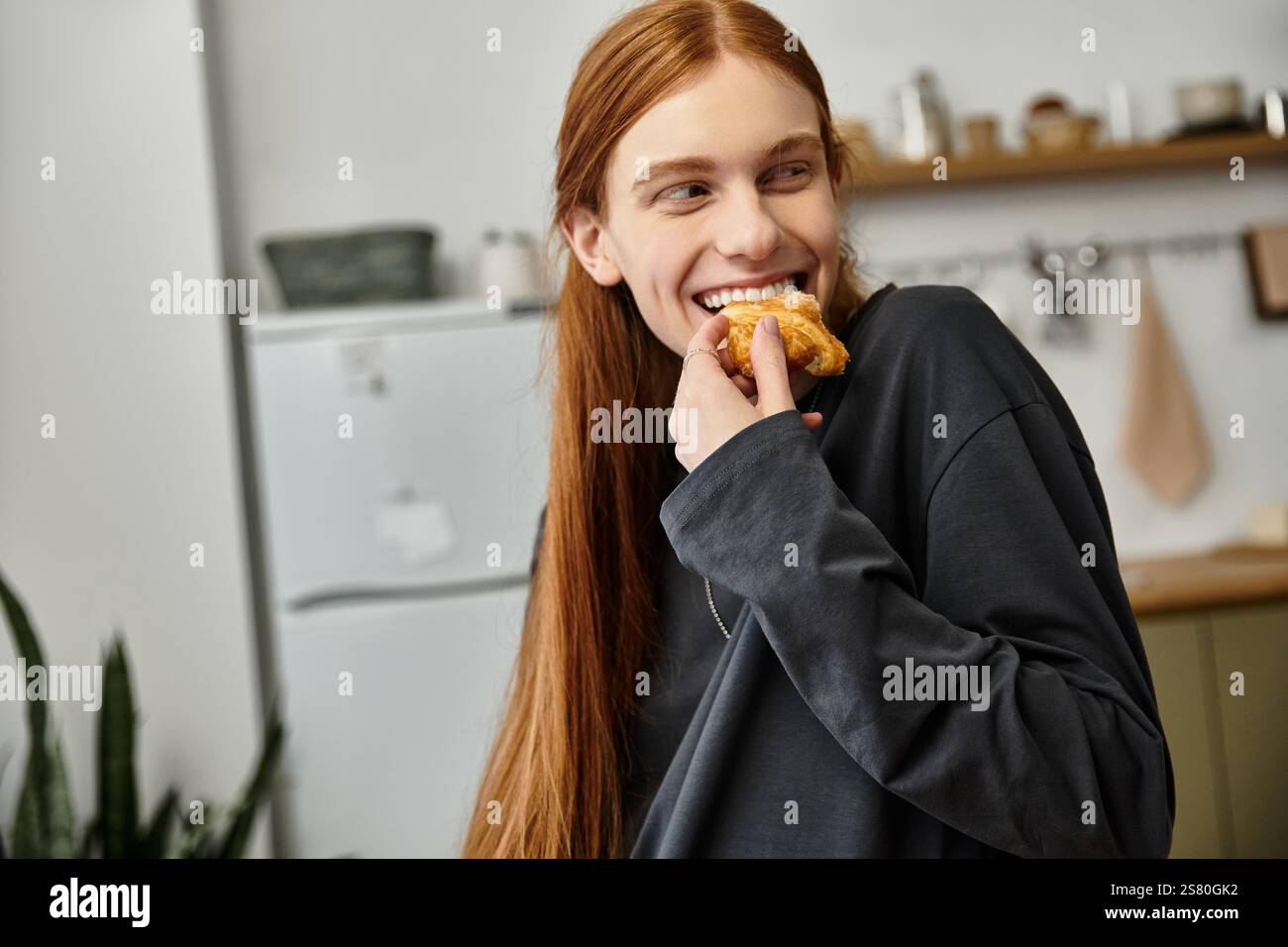 A good looking young guy with long hair smiles while eating a snack in ...