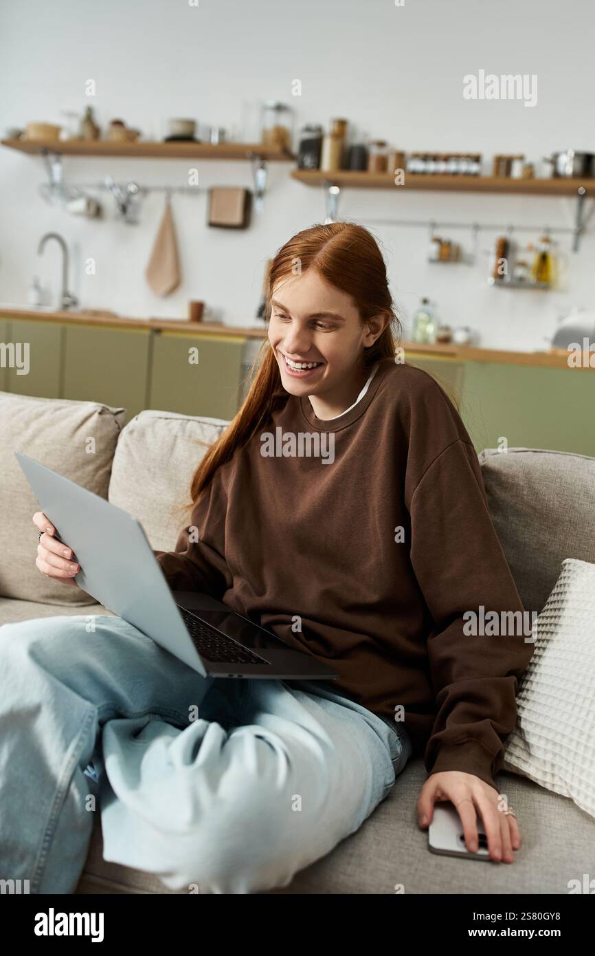 A young guy with long red hair relaxes in his stylish apartment while using a laptop. Stock Photo