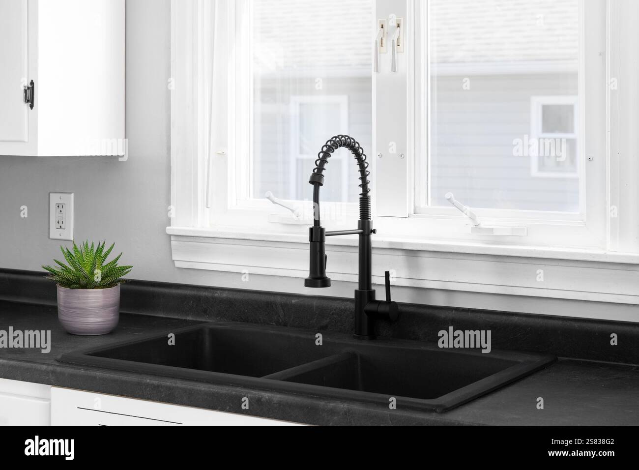 A modern white kitchen with a black stone double sink and black faucet ...