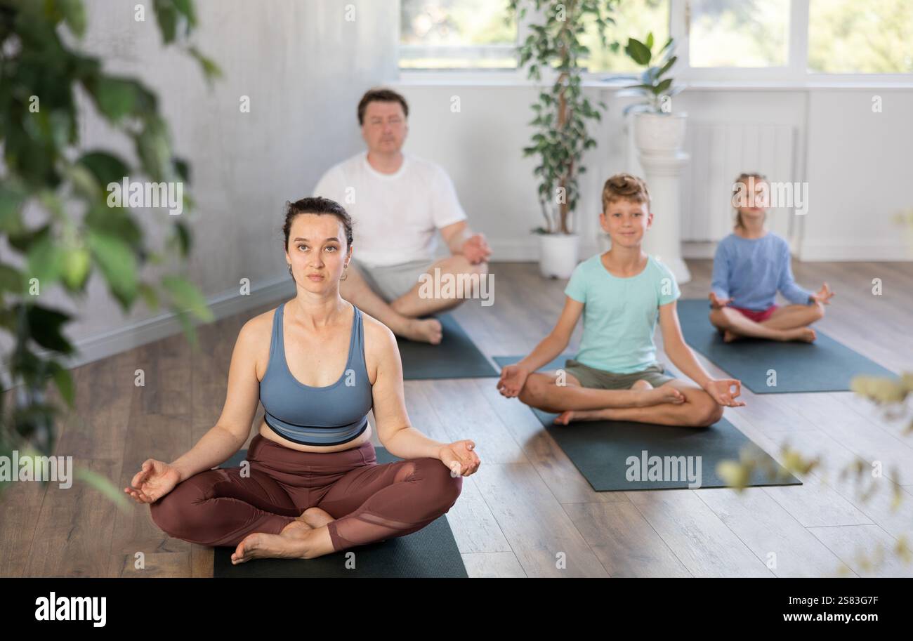 Positive middle-aged woman practicing lotus pose of yoga with her ...