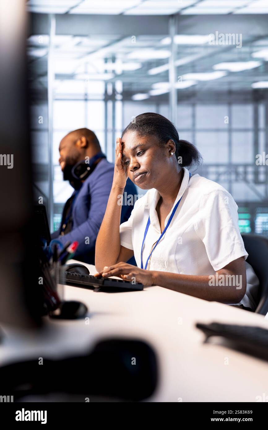 Data center technician feeling headache from stress while using programming languages on PC. Fatigued server farm worker debugging and optimizing code, feeling overworked Stock Photo