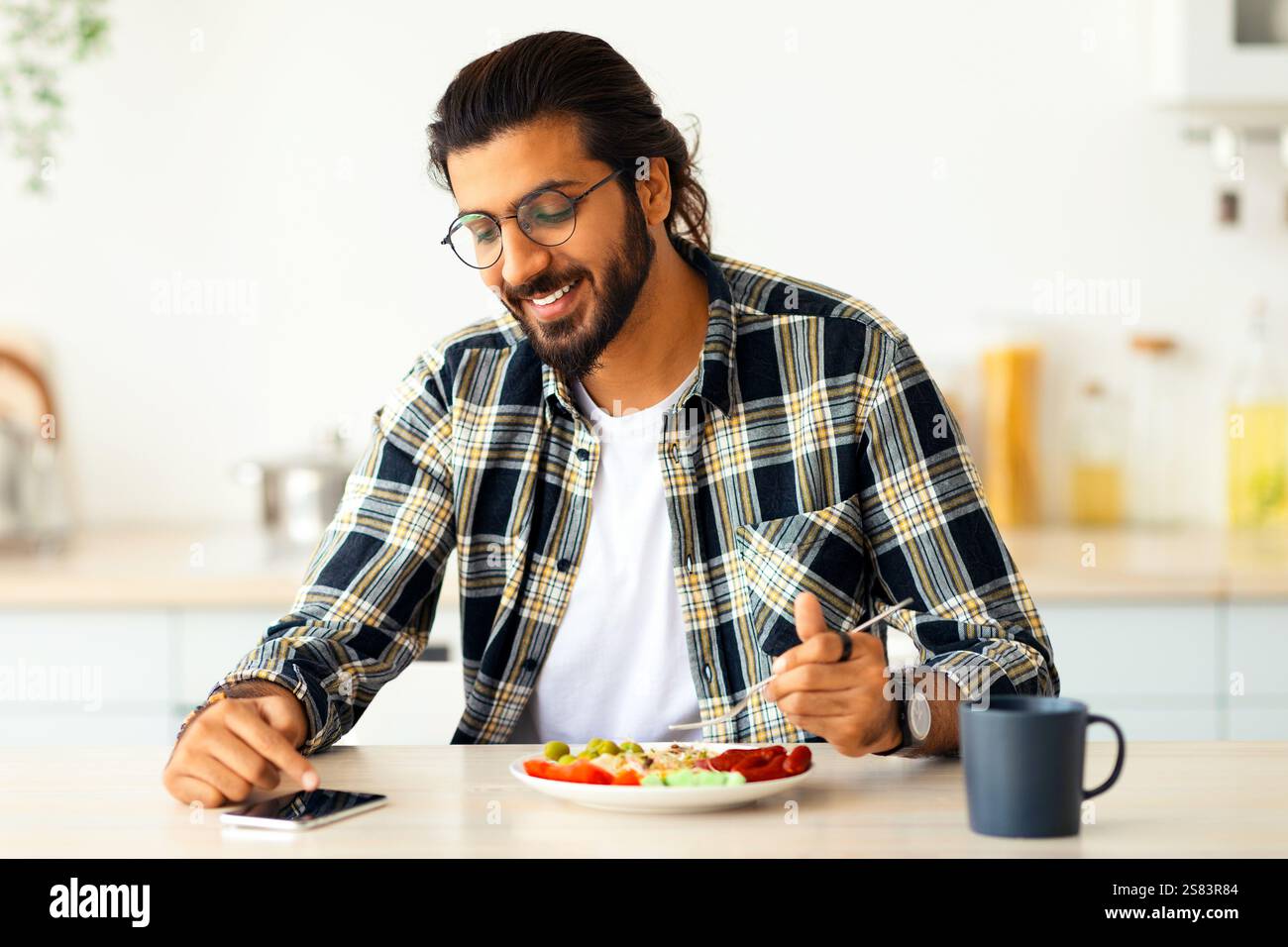 Handsome indian man using cellphone while having breakfast Stock Photo