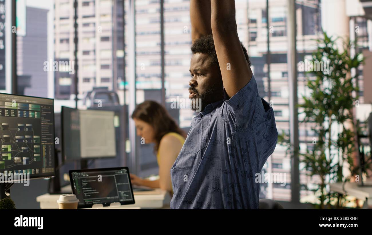 System administrator in pain, suffering muscle sprain while developing machine learning APIs. Man feeling backache from sitting at desk all day while training predictive models Stock Photo