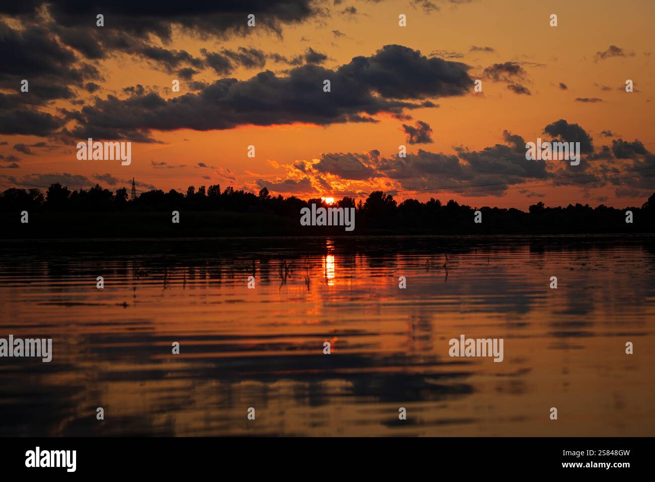 The sun sets behind scattered clouds, casting orange and red hues ...