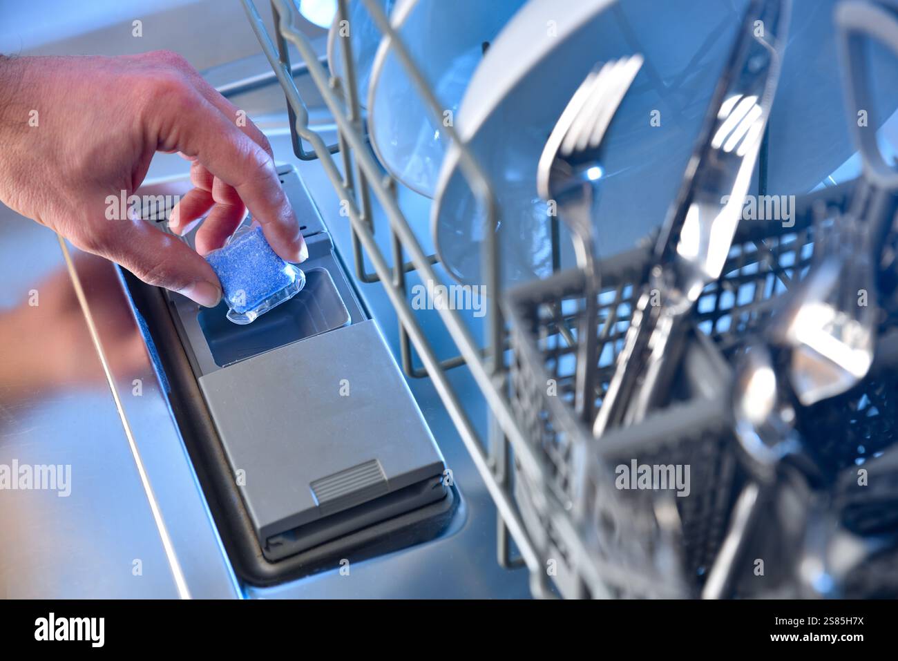 Hand inserting a dishwasher detergent tablet into the door compartment ...