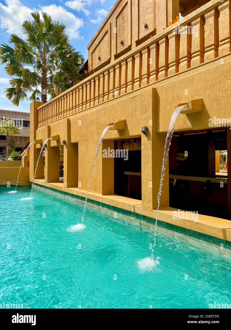 Modern Tropical Pool with Water Fountains and Palm Trees    A modern tropical pool with cascading water fountains, surrounded by yellow architecture - Smartphone Captured Stock Image