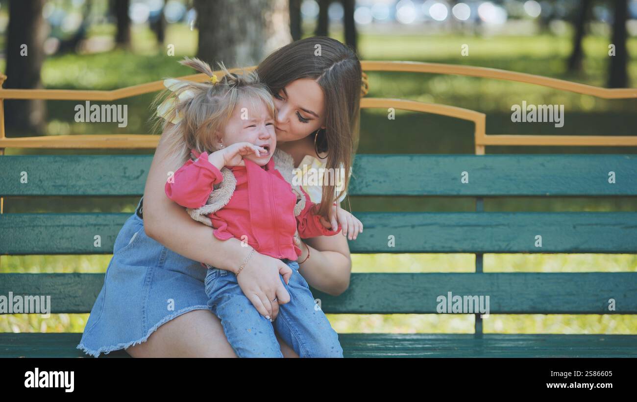Caring mother comforting tearful child on sunlit park bench, nurturing ...