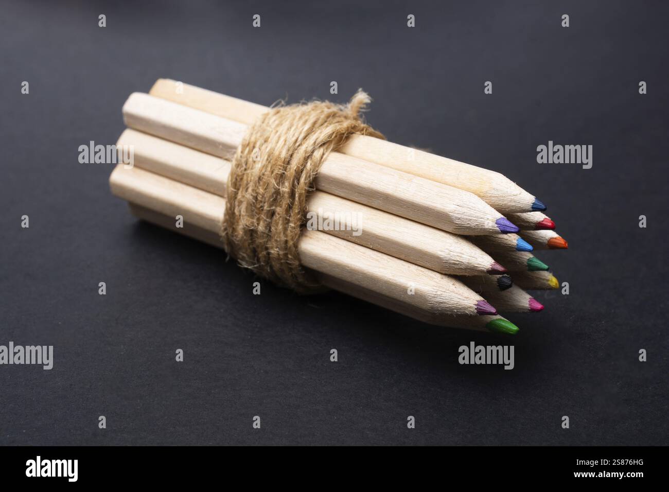 Bundle of colored pencils wrapped with string on black Stock Photo