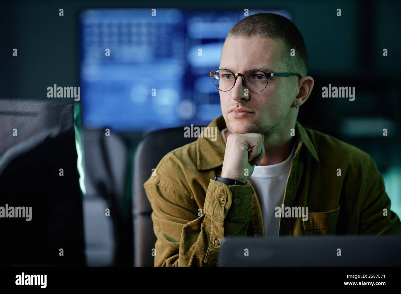 Portrait of thoughtful male software developer reading computer screen with attention solving code problem while working in evening hours in IT company office, copy space Stock Photo