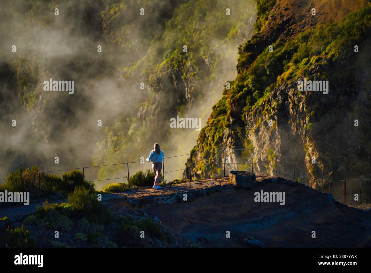 Hikers on trail pathway along jagged volcanic cliffs on Pico Areeiro with cloud inversions blowing over mountain peaks, Madeira island, Portugal. Stock Photo