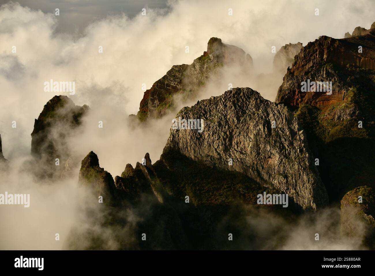 Mountains with pathway along jagged volcanic cliffs on Pico Areeiro with cloud inversions blowing over mountain peaks, Madeira island, Portugal. Stock Photo