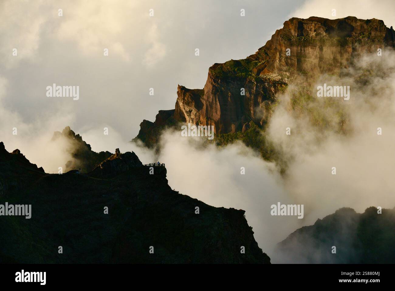 Mountains with pathway along jagged volcanic cliffs on Pico Areeiro with cloud inversions blowing over mountain peaks, Madeira island, Portugal. Stock Photo