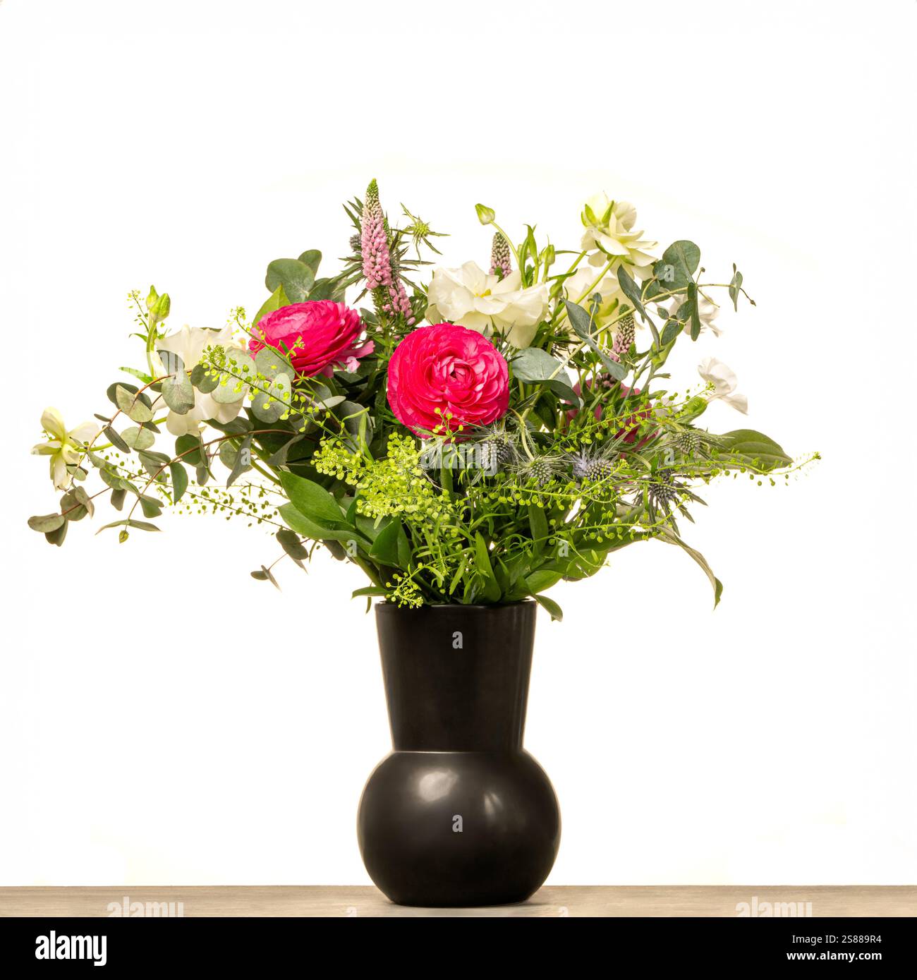 Black vase with pink and white flowers, and foliage seen against a white background. Stock Photo