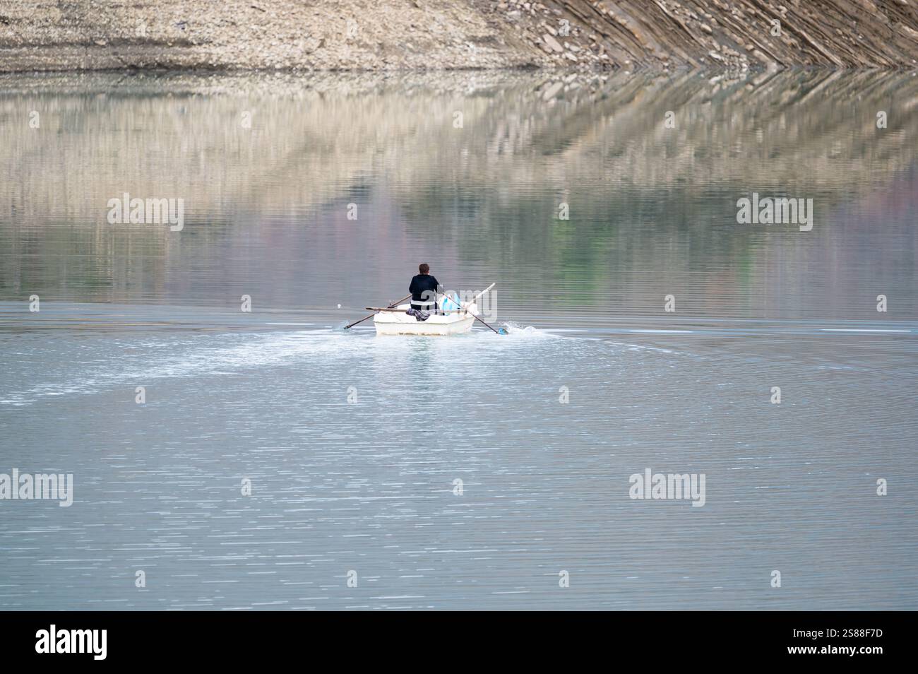 Middle aged local lady on a rowing boat, crossing the Bovilla lake, Albania, DEC 12, 2024 Stock Photo