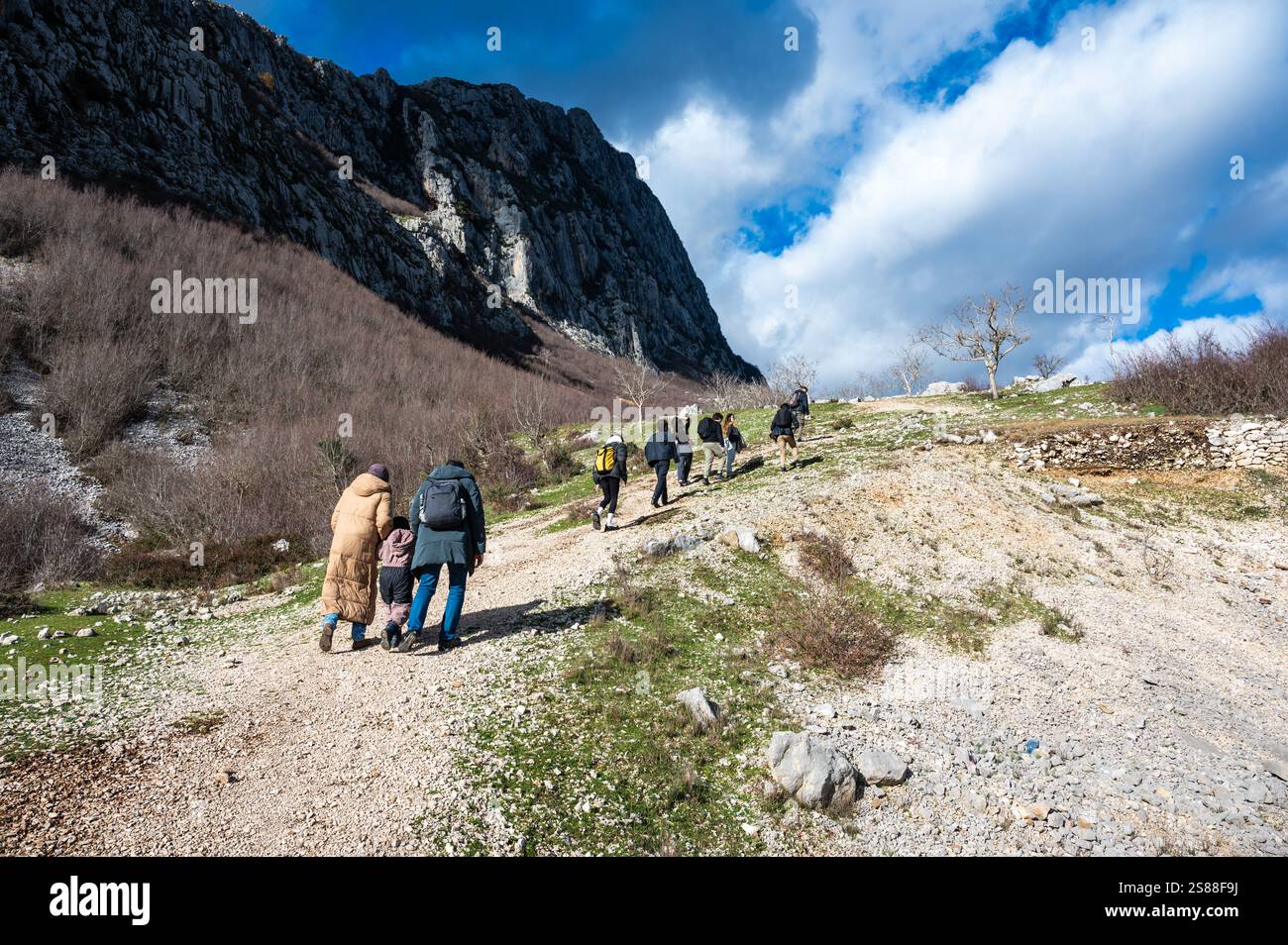 Mixed group of tourists walking a dirty gravel road on the Gamti Mountain in Albania, DEC 12, 2024 Stock Photo