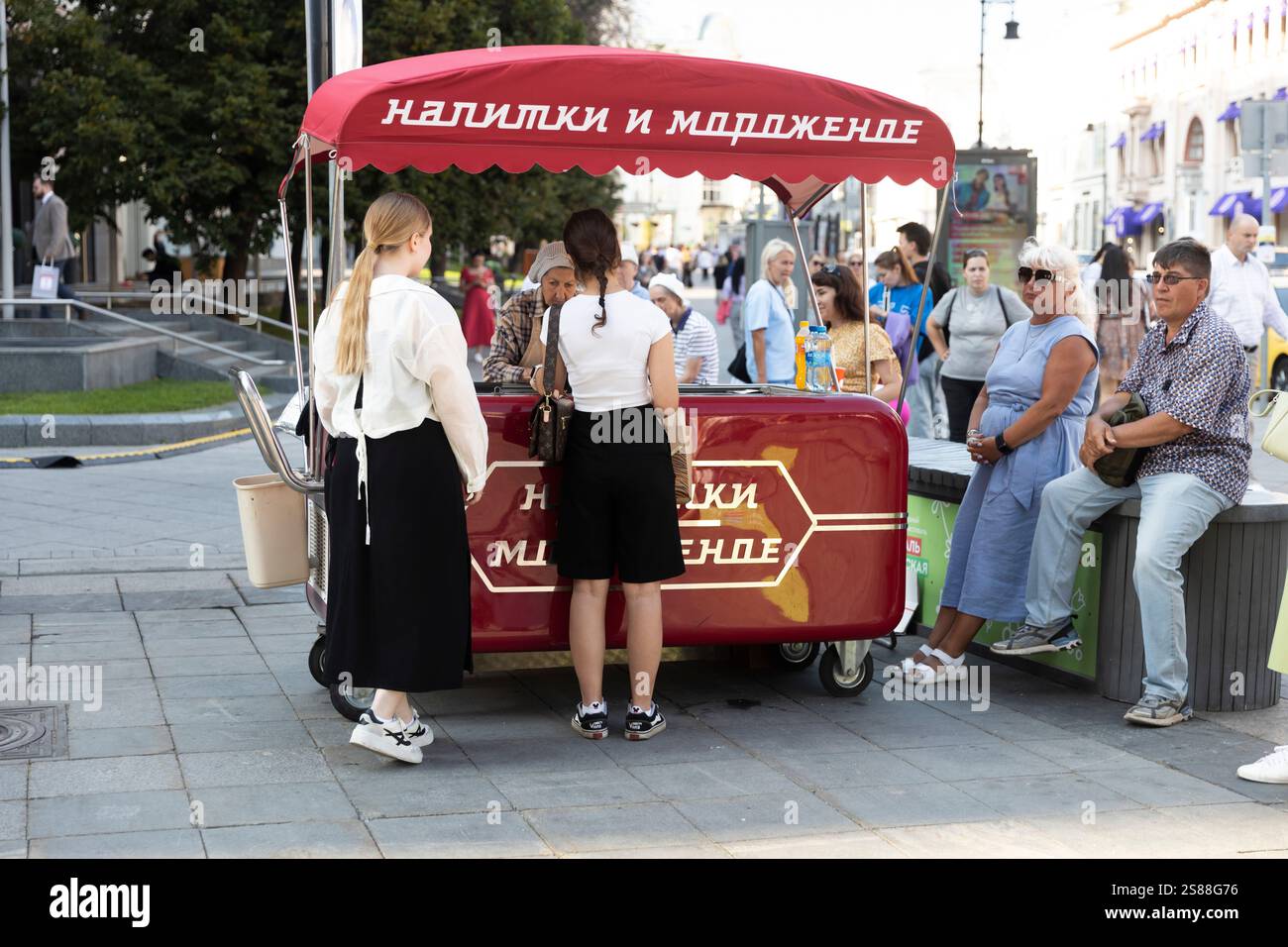 Moscow, Russia - August 25, 2024, A vendor at the street kiosk 'Drinks and Ice Cream' sells products to girls near the TSUM store. Stock Photo