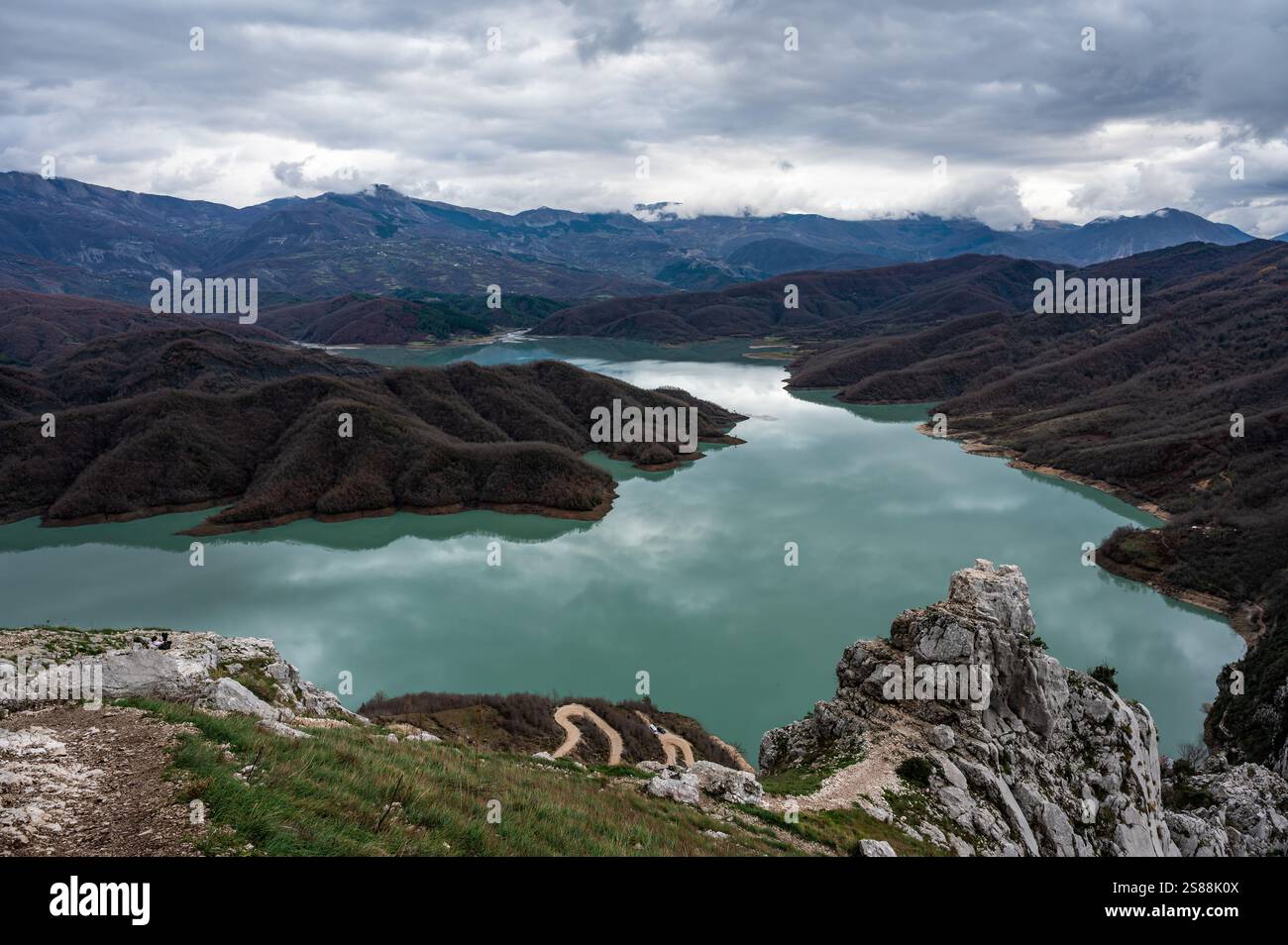 Scenic panoramic view over the Gamti mountains and Bovilla lake with colorful begetation, blue water and an overcast sky, Albania Stock Photo