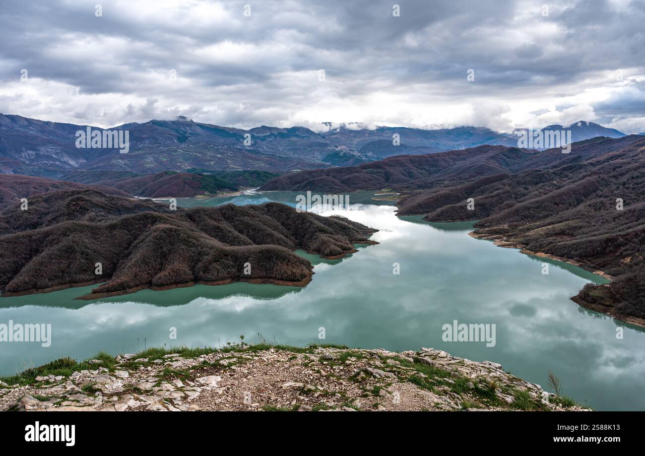Scenic panoramic view over the Gamti mountains and Bovilla lake with colorful begetation, blue water and an overcast sky, Albania Stock Photo