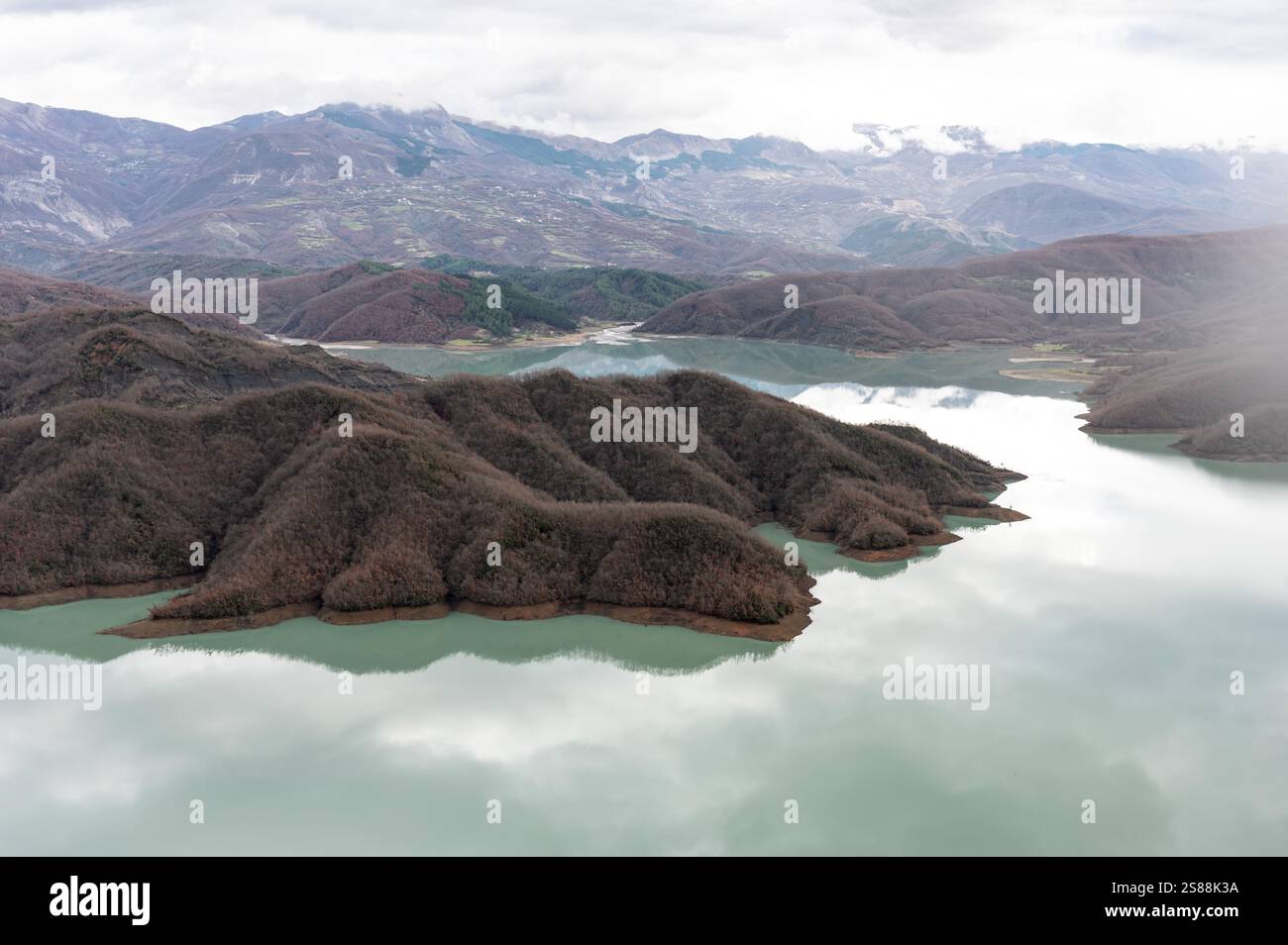 Scenic panoramic view over the Gamti mountains and Bovilla lake with colorful begetation, blue water and an overcast sky, Albania Stock Photo