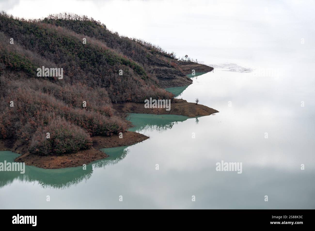 Reflections of mountain slope and brown soil with green vegetation in the Bovilla lake, Albania Stock Photo
