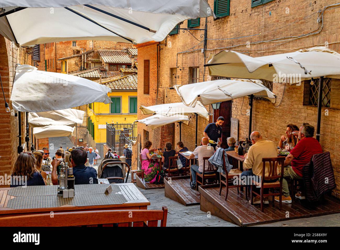People sitting down eating at two restaurants which are side by side on Costa Sant'Antonio a very steep narrow street in Siena ,Italy Stock Photo