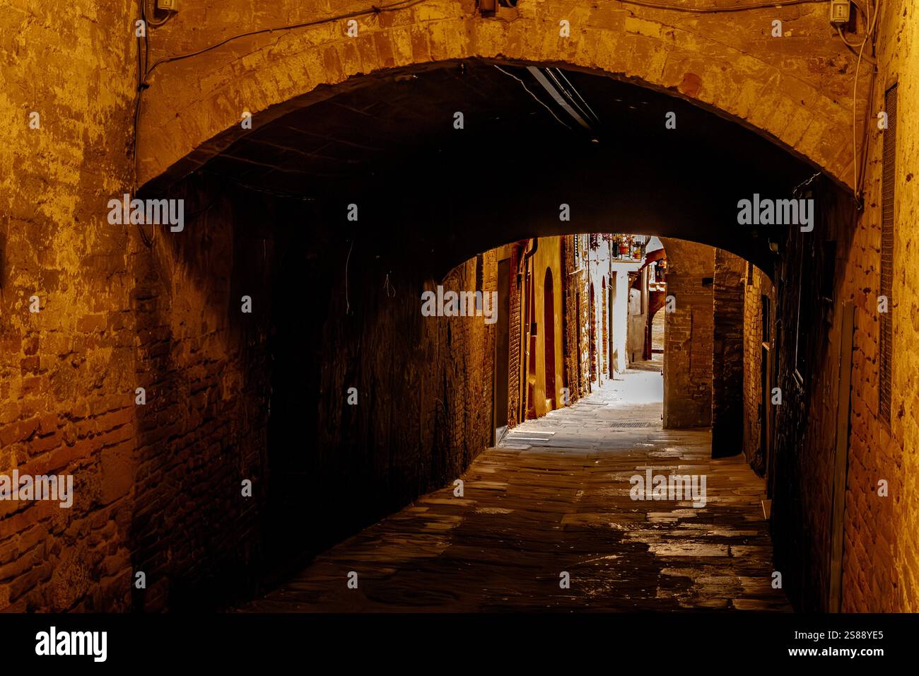 A narrow street leading under an archway in the medieval city of Siena,Italy Stock Photo