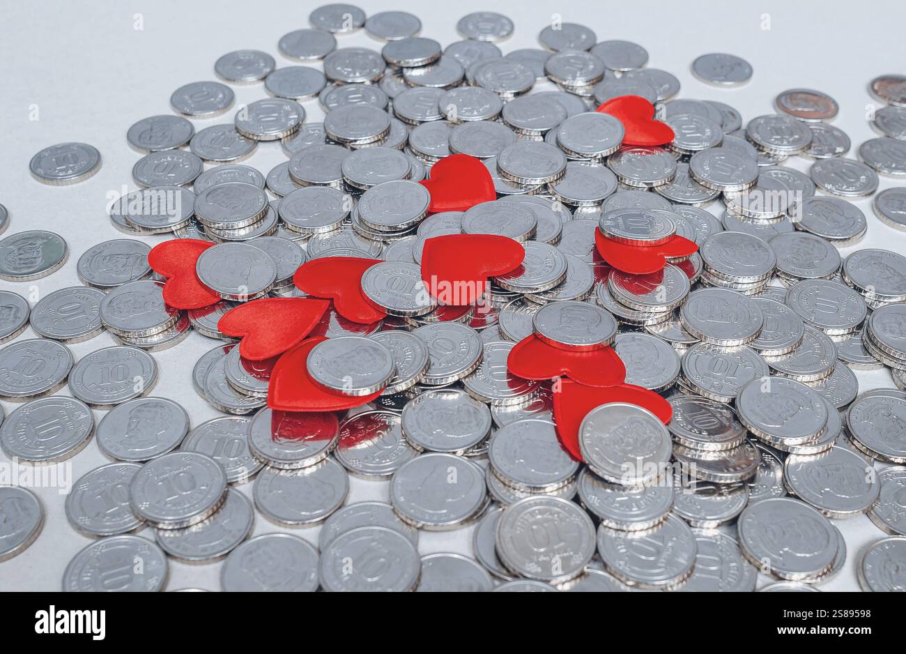 Scattered silver coins and several red hearts isolated on grey. Idea for design. Valentine's Day card Stock Photo
