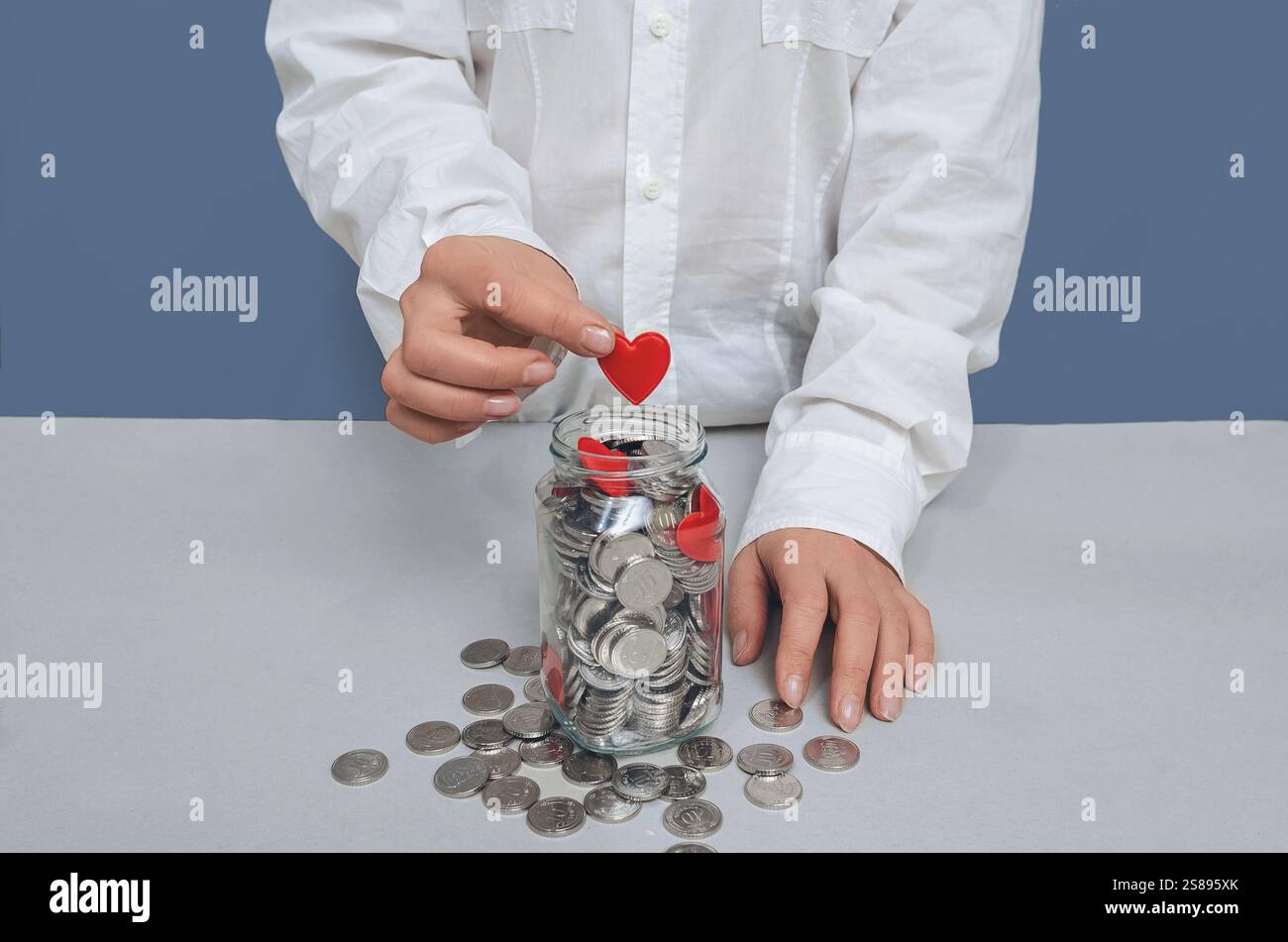 Donation jar with silver coins, into which hand of woman in white shirt ...